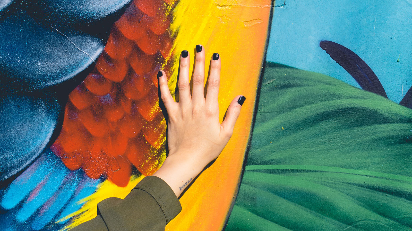 A hand with black painted nails laid flat over a brightly painted mural.
